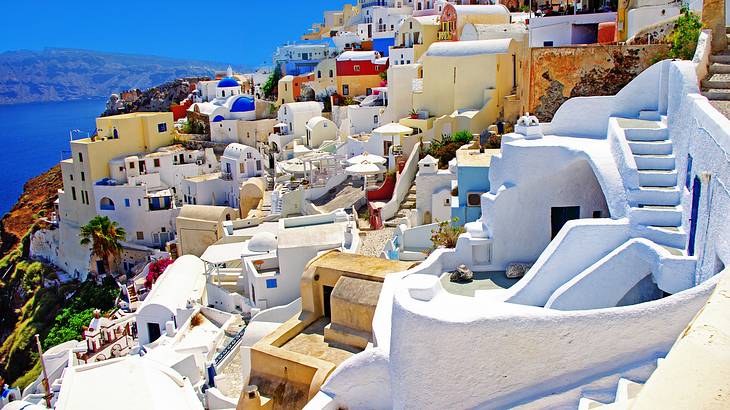 White houses built on a hill next to the water and a mountain range in the distance