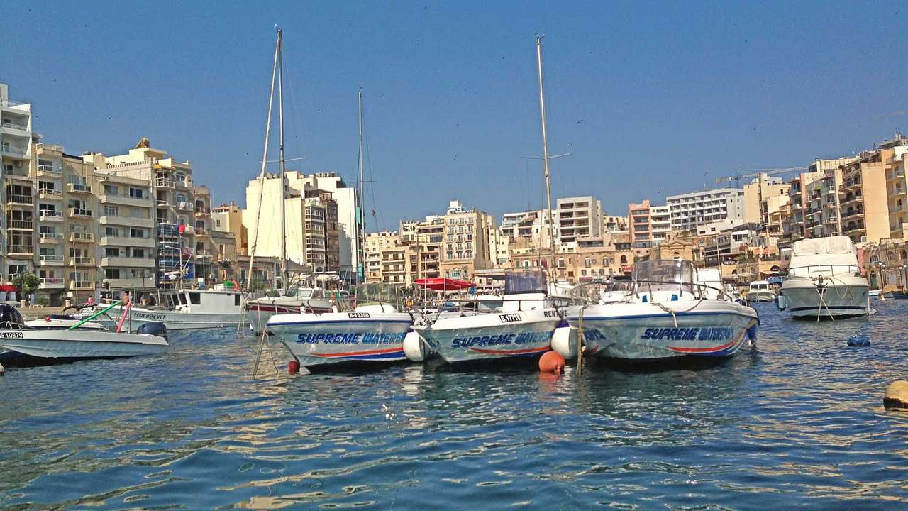 A marina with boats in it surrounded by buildings under a blue sky