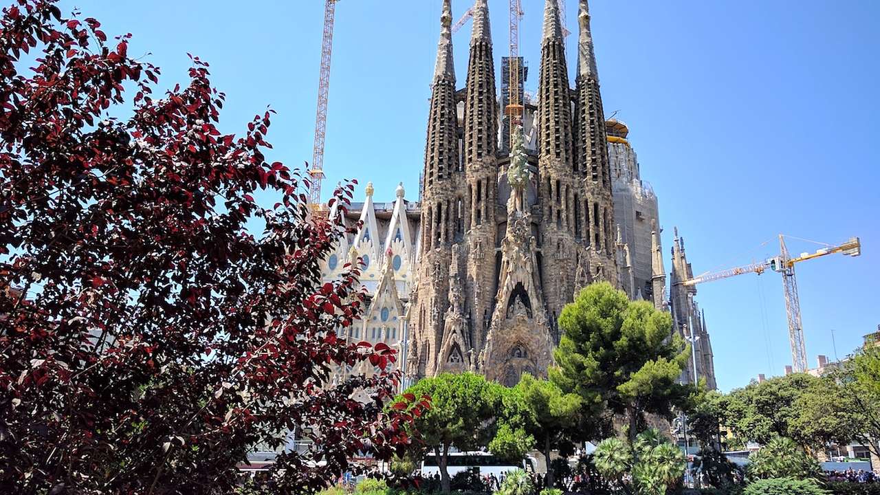 A tall cathedral with many spires next to red and green trees