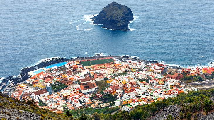 Aerial view of a town next to a body of water with a rock in the middle