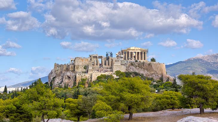 A historic stone monument on a hill surrounded by greenery, and a partly cloudy sky