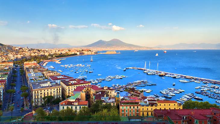 Buildings built along the coast with a harbor, boats, and a mountain range