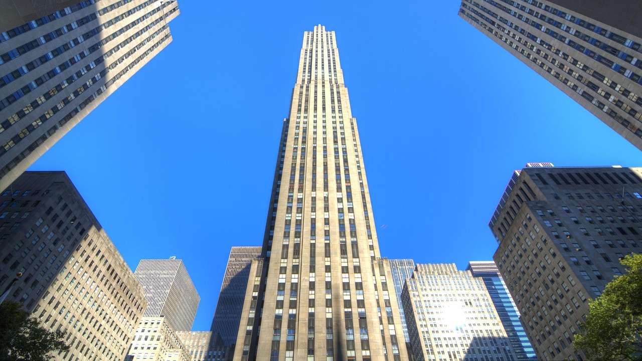 Looking up at a tall concrete building with lined-up windows against a clear blue sky
