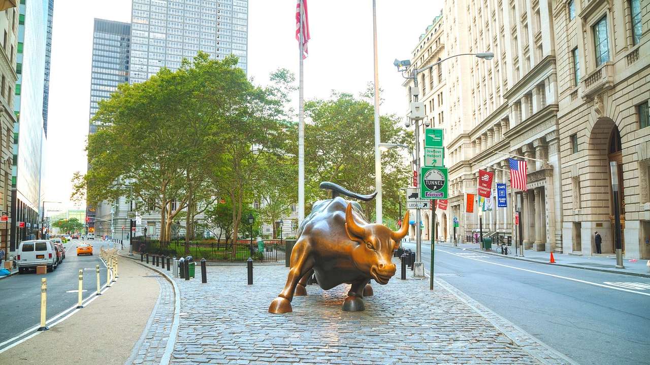 A bronze sculpture of a bull on a cobbled pavement between two roads