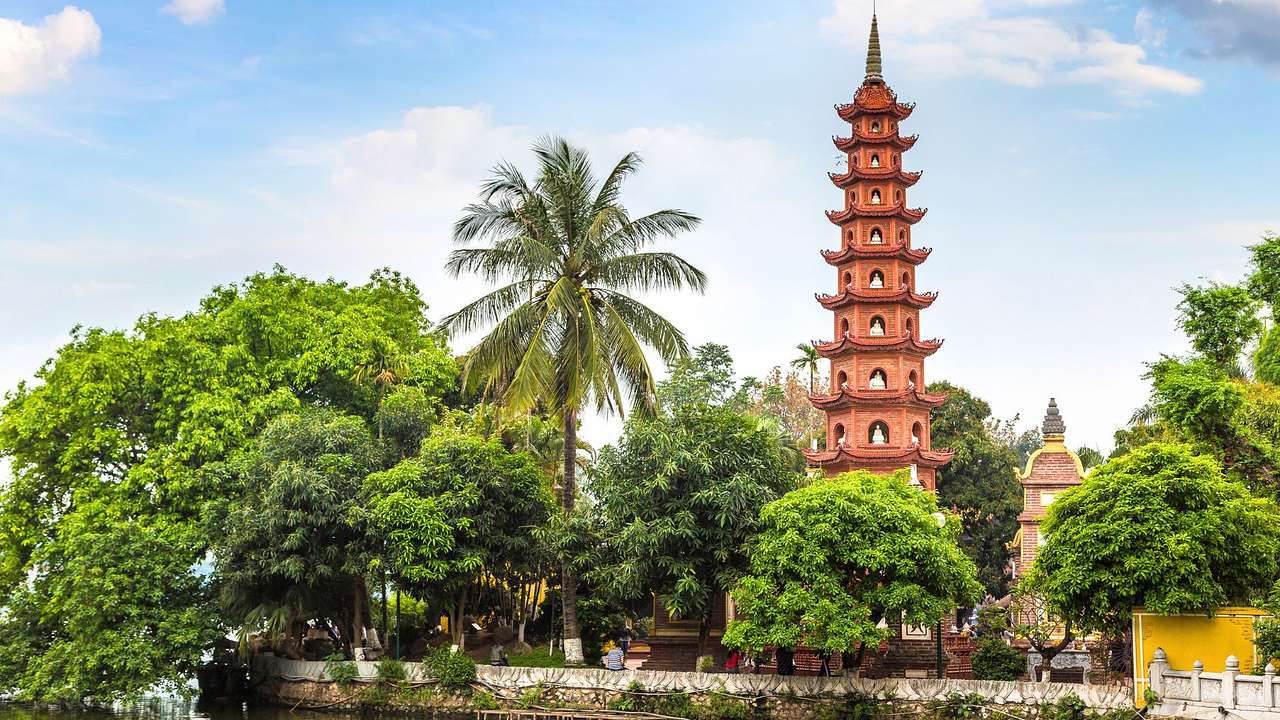 A multi-tiered pagoda next to many green trees and a blue sky with clouds