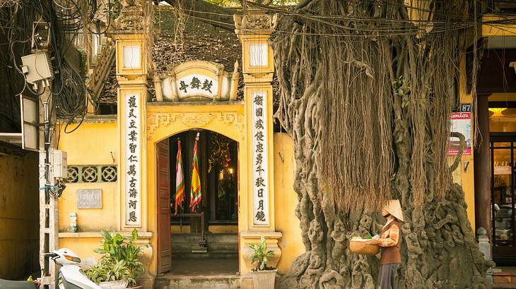 A yellow temple with an arched gate and Vietnamese writing next to the street