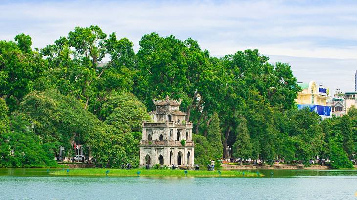 A three-story ancient tower with green trees behind it and a lake in front