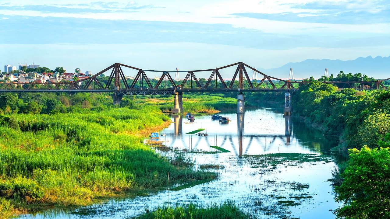 A steel bridge across a body of water with greenery around it