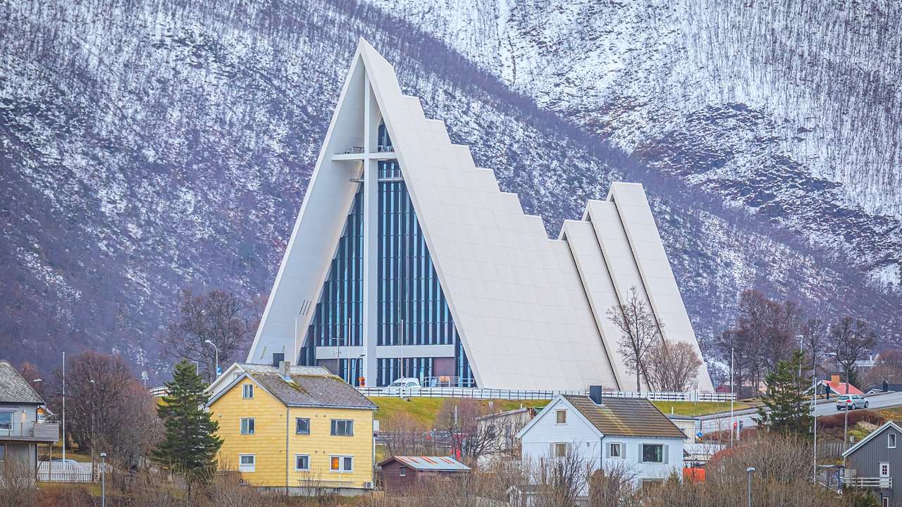 A triangular-shaped building with a cross next to a snow-covered mountain