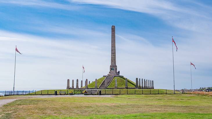 A tall obelisk monument with smaller stones around it next to the grass and flags