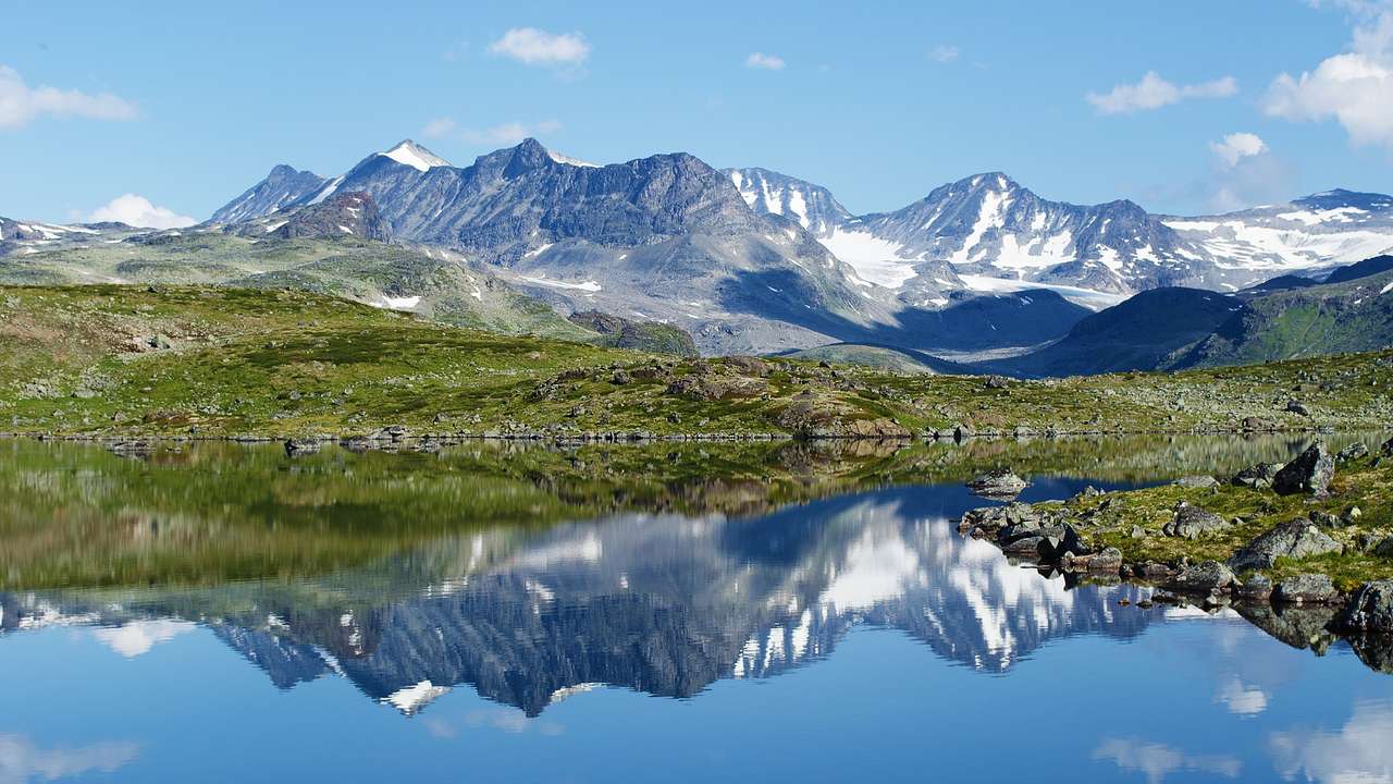A lake next to snowy mountains that reflect in the surface