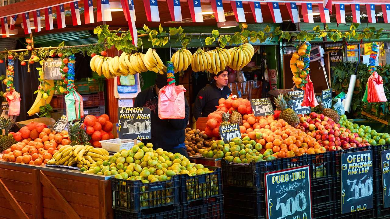 A market stall with lots of colourful fruit, and red, blue and white flags above