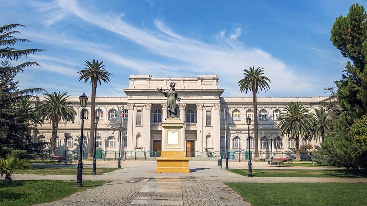 A stone building with a statue in front of it, on a path next to grass and palm trees