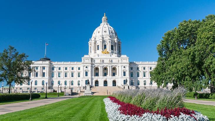 A large white building with a dome structure next to a garden with flowers and grass