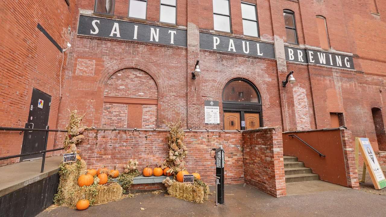 A red brick building with a "Saint Paul Brewing" sign and an autumn display in front