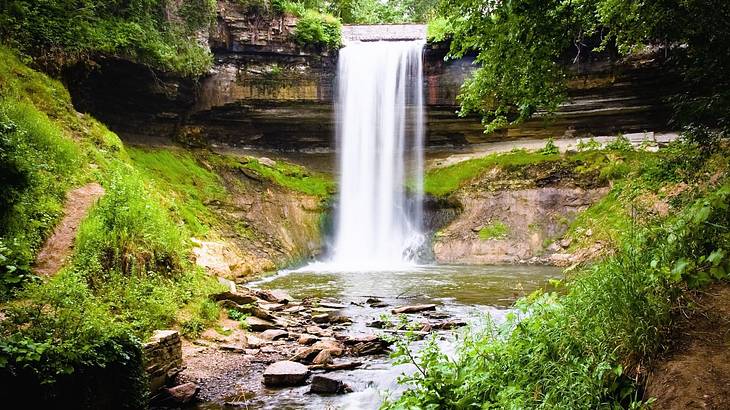 A waterfall flowing into a pond with rocks and greenery around it