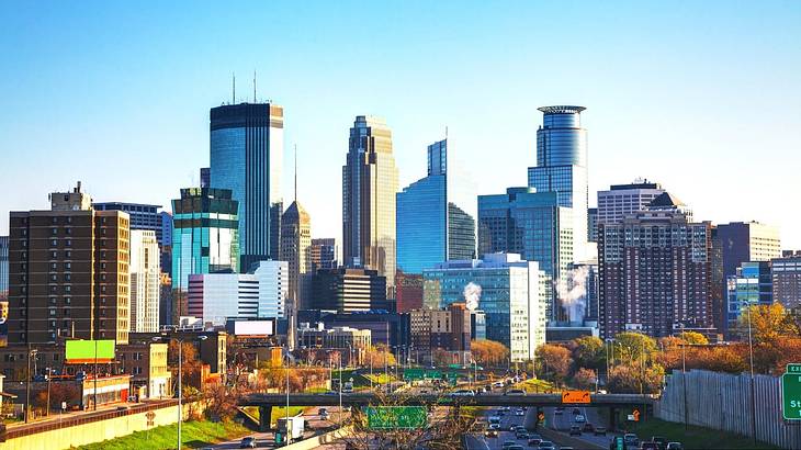 A city skyline with mirrored buildings next to a highway under a blue sky