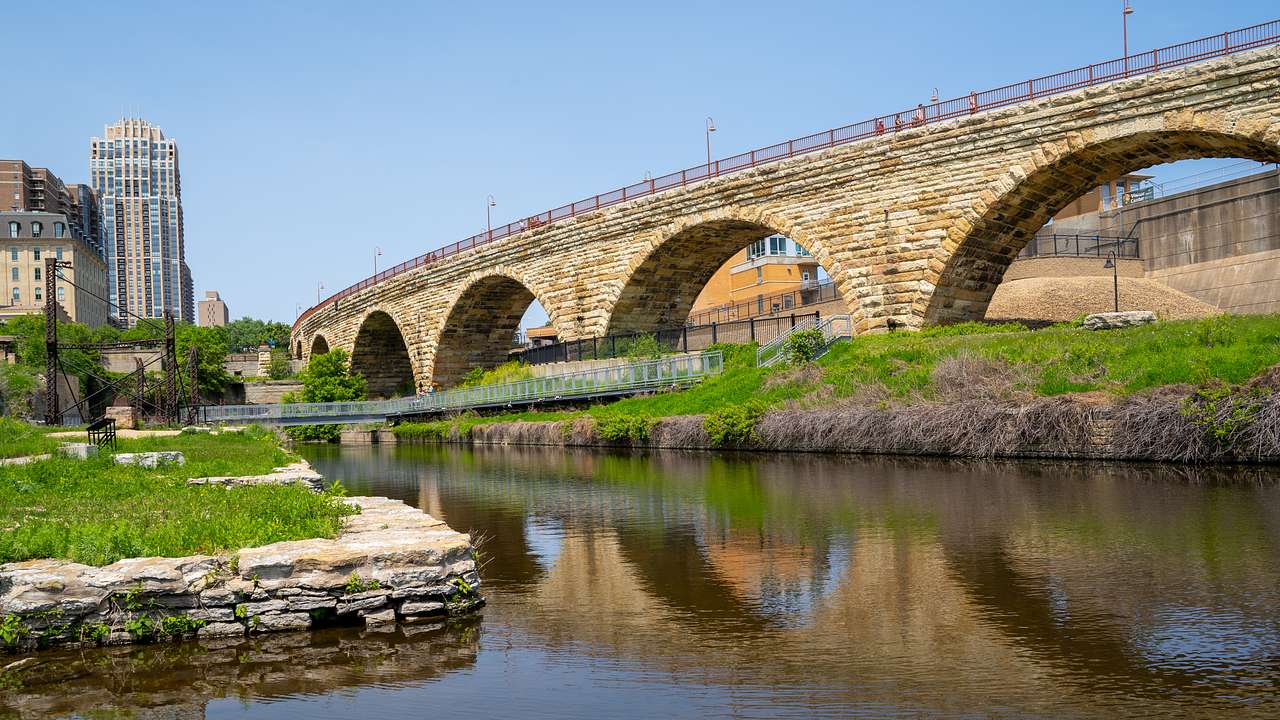 An arched stone bridge over water with tall buildings to the side