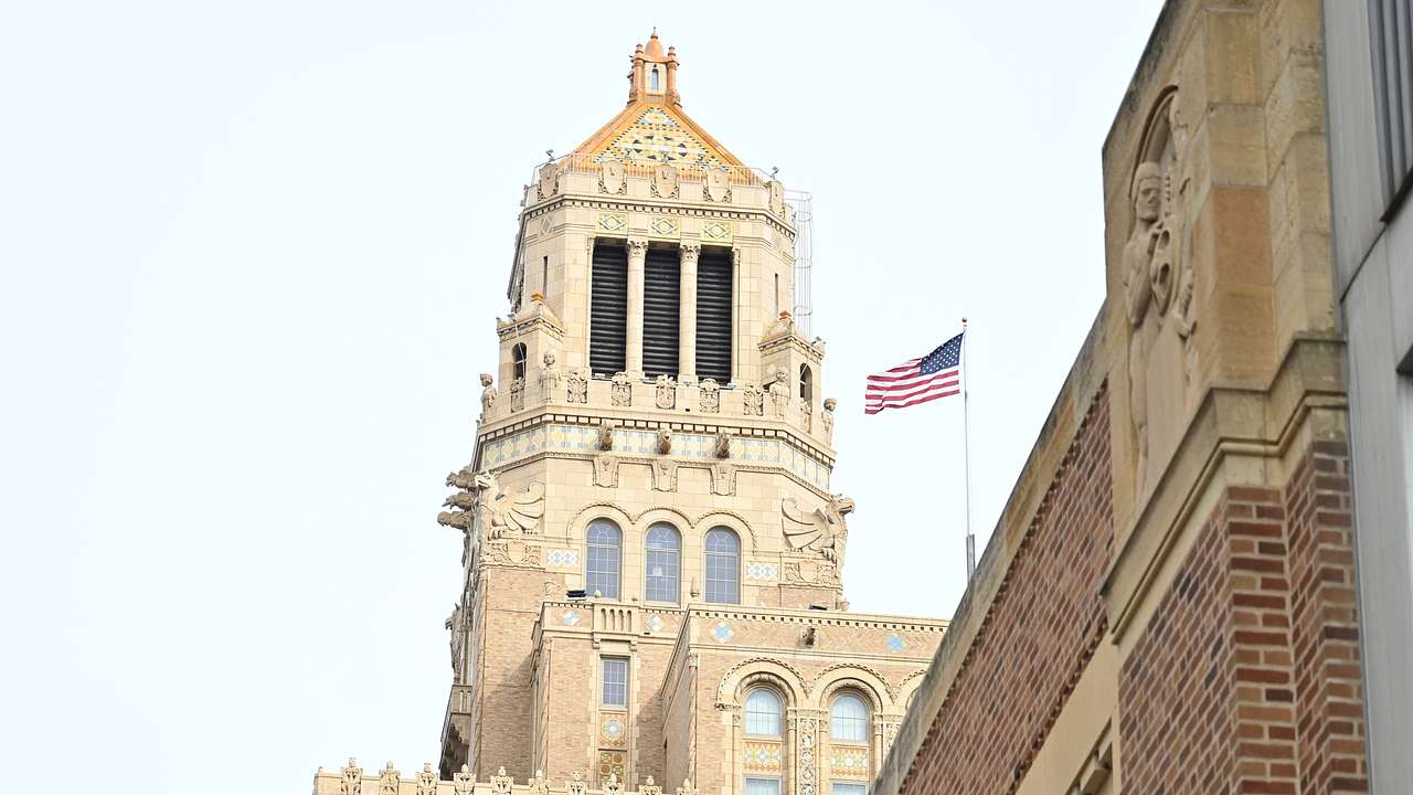 A tall stone tower on top of a building with the USA flag flying in the wind