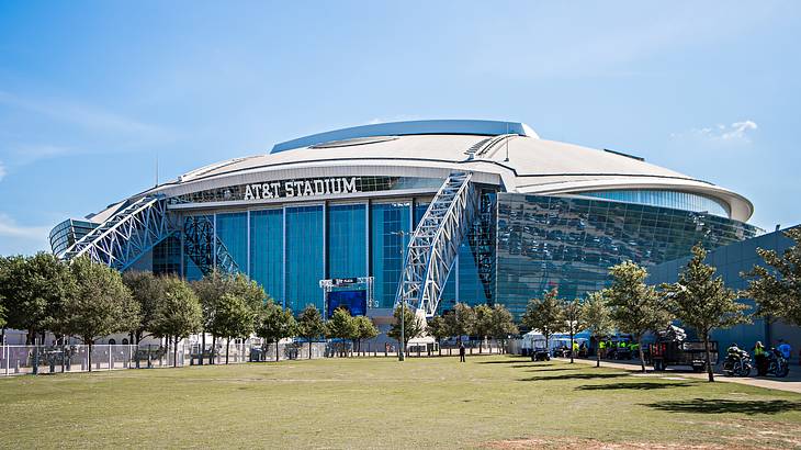 A football stadium that says "AT&T Stadium" with grass and trees in front of it