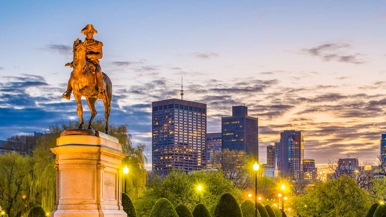 A statue of a man on a horse in a green park at night with buildings behind