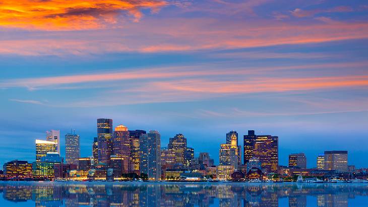 View of a lit-up city skyline from the water at sunset