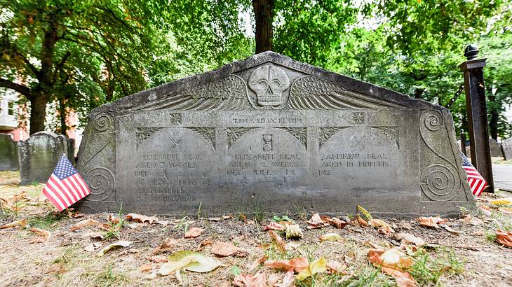 A grave headstone with a skull and engravings on it, with American flag in front