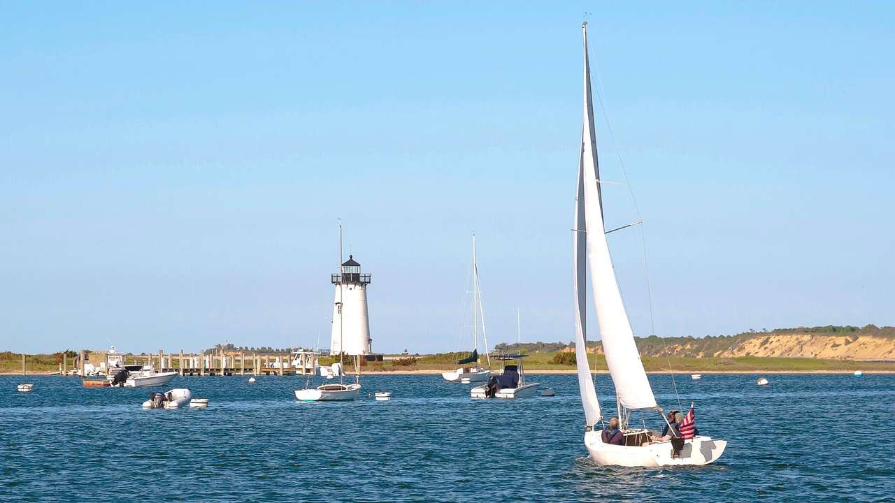 A sailboat on the water with a lighthouse on the shore