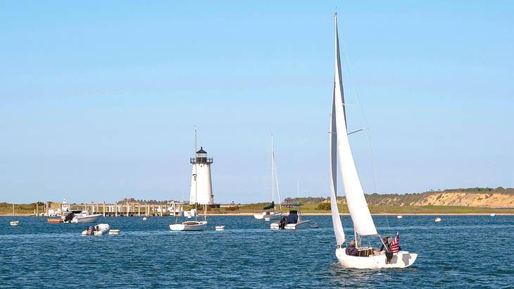 A sailboat on the water with a lighthouse on the shore