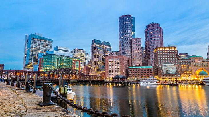 A modern city skyline next to a harbor and a cobblestone path at sunset