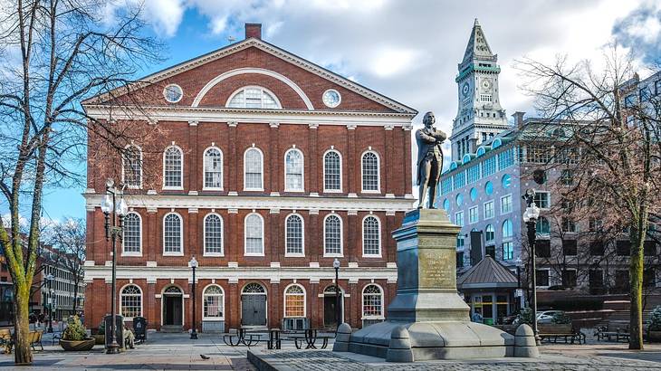 A red brick building with lots of windows with white frames next to a statue