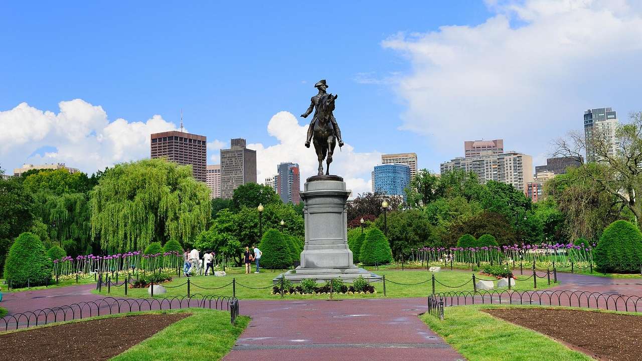 A park with a path, grass, and at trees, and a statue of a man on a horse