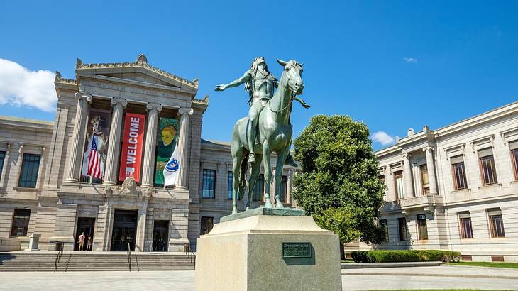 A stone museum building with a statue and grass in front of it