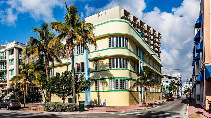 A yellow Art Deco building on a street corner with palm trees in front