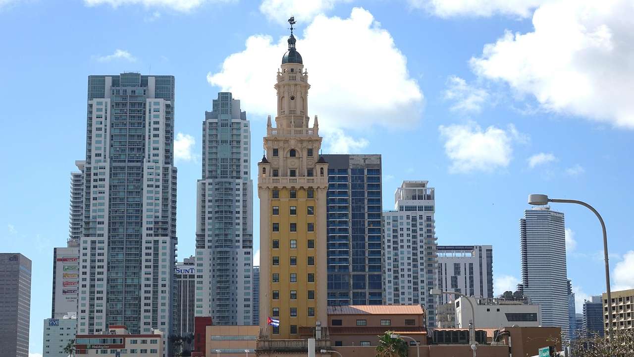 A yellow tower with skyscrapers behind under a blue sky with clouds