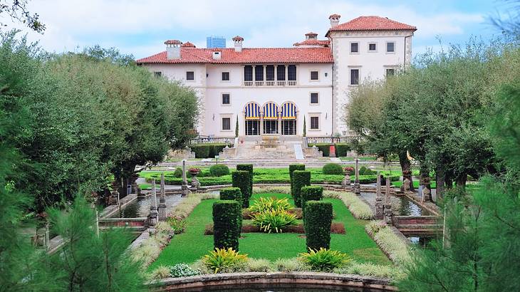 A villa-style house with manicured green gardens and a pond in front under blue sky