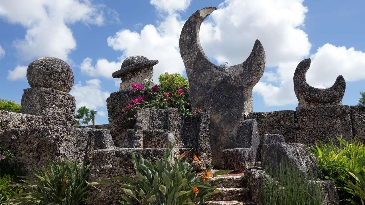 A garden with stone sculptures under a blue sky with clouds