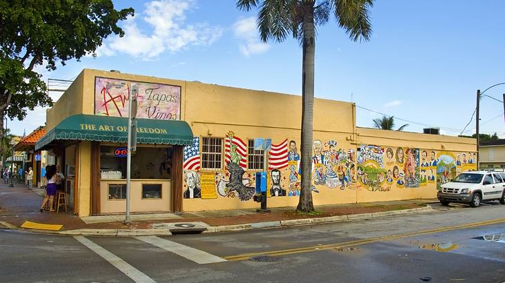 A yellow building with green awning and murals on the side with a road in front