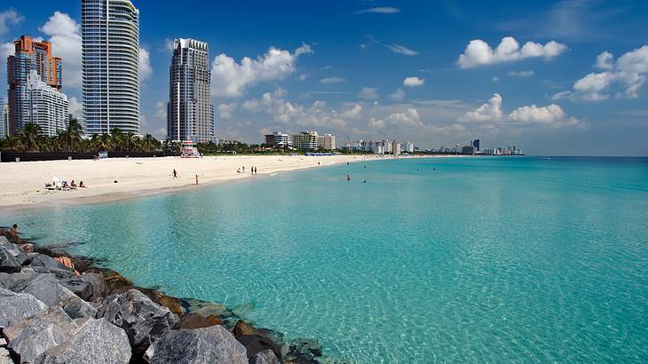 Blue ocean and sandy beach with skyscrapers in the background and rocks on the left