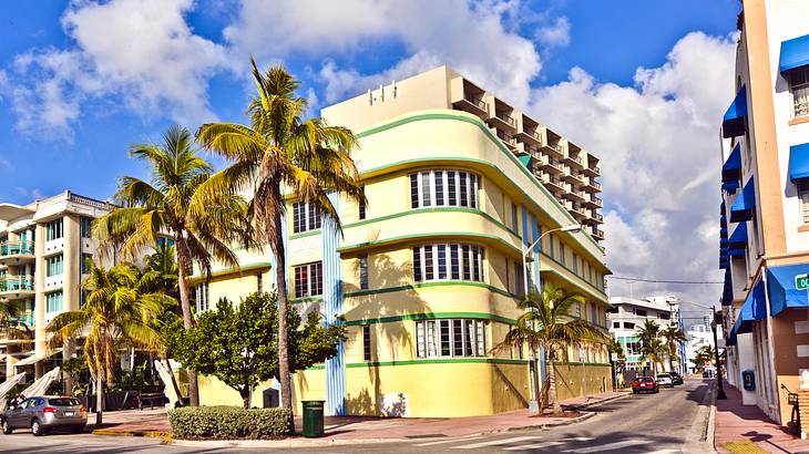 A yellow Art Deco building on a street with palm trees in front of it