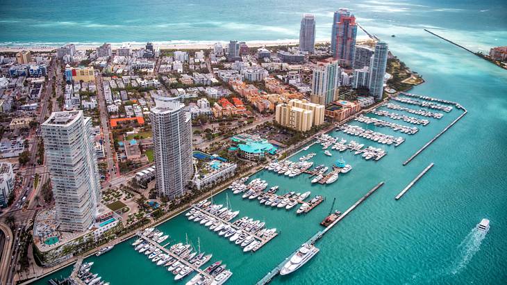 An aerial view of a marina with water and boats and a city skyline to the side