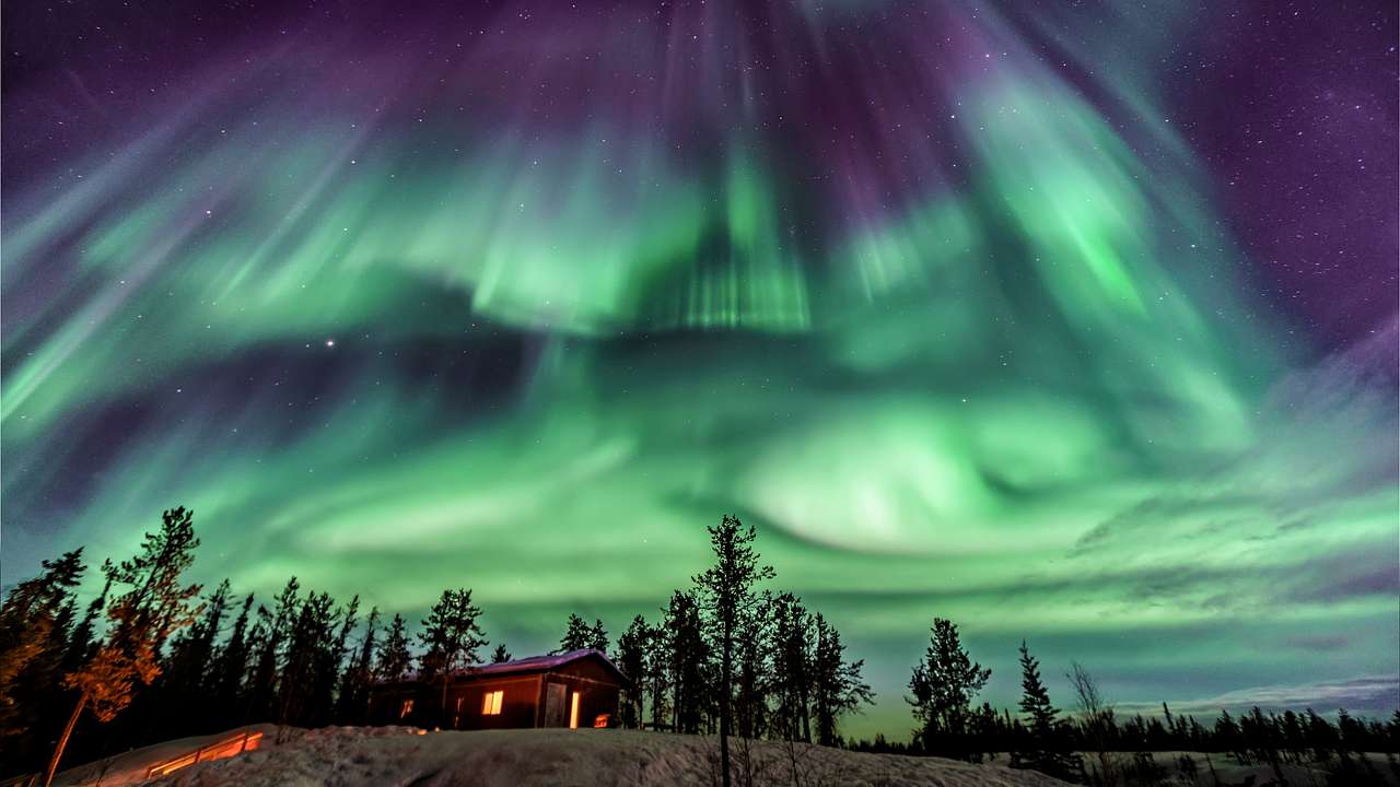 Northern lights over a small wooden house near trees