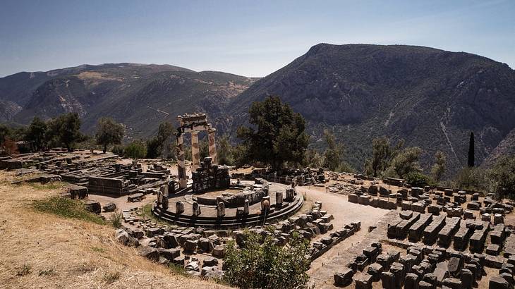 Bird's-eye view of ancient Greek ruins and a temple with mountains at the back