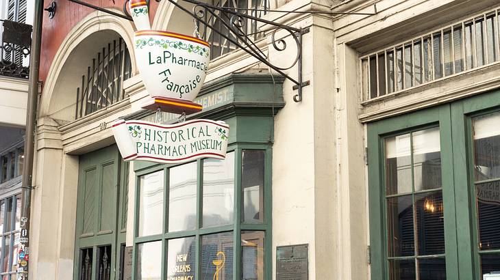 A white building facade with green doors and windows with a hanging sign