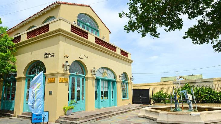 A yellow building with green shutters next to a fountain and trees