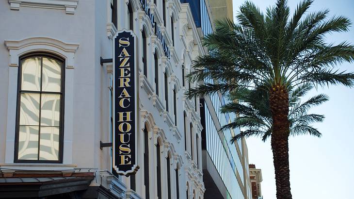 A side of a white building with a sign saying "Sazerac House" near a palm tree