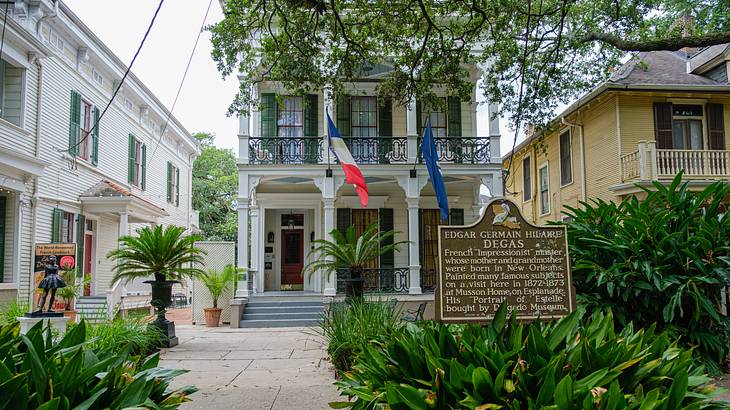 A house with a hanging flag near other structures and plants