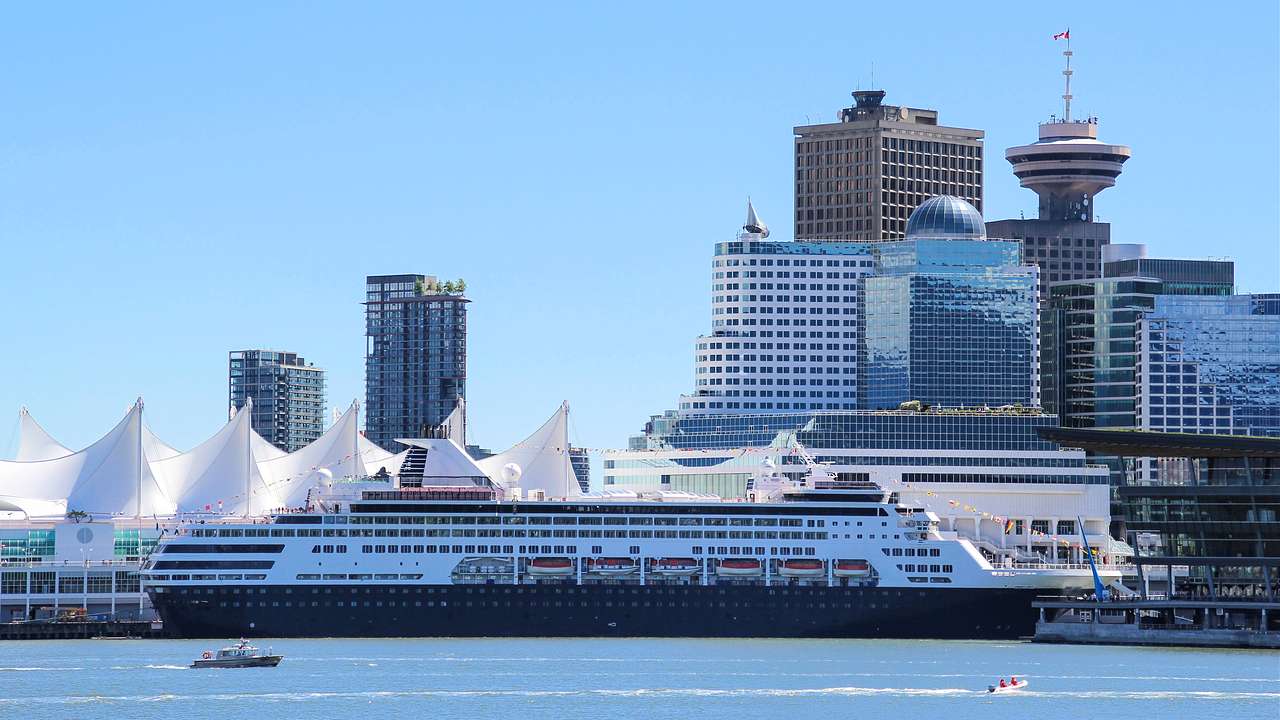A cruise ship docked by a harbor near modern buildings
