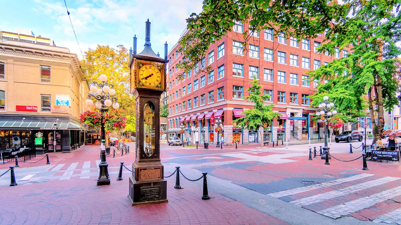 A steam clock in a corner of a street near buildings and trees in the autumn