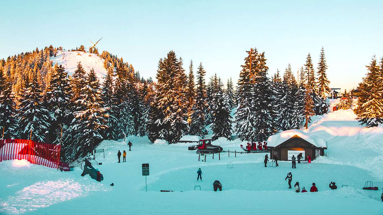 Sunrise over a snowy mountain top with trees, skiers, and a cabin